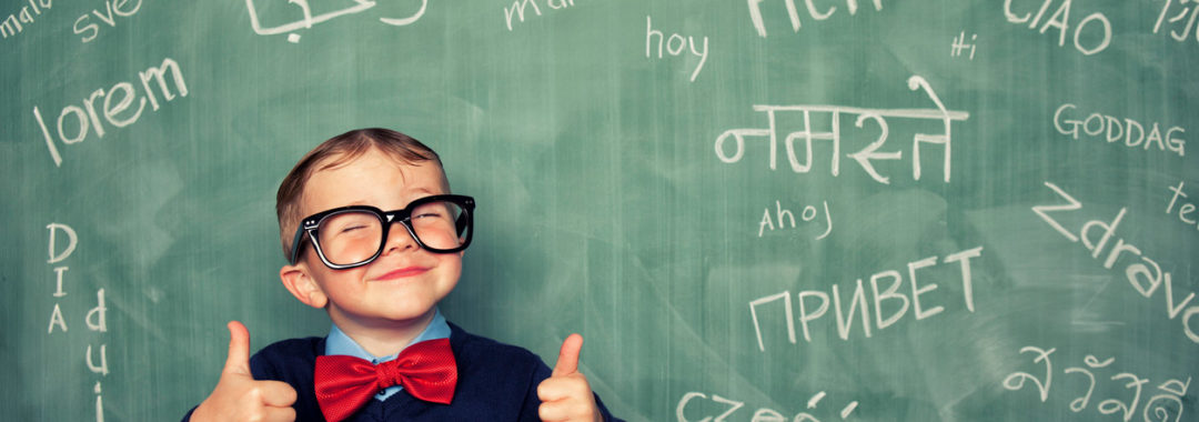 A young child smiling in front of a chalkboard filled with words in different languages