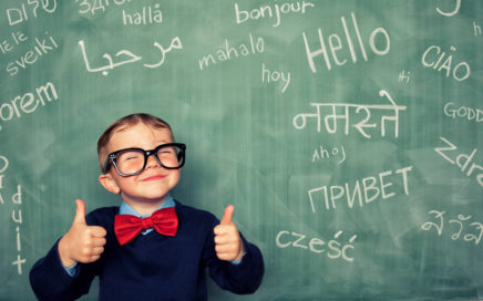 A young child smiling in front of a chalkboard filled with words in different languages